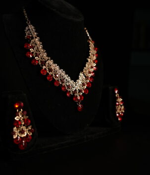 Rose gold ruby red crystal floral necklace and chandelier earring bridal jewellery set displayed on black velvet bust