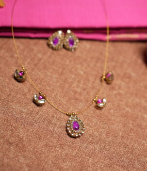Kundan invisible wire necklace with floating purple gemstone and pearl pendants displayed on pink silk fabric with matching earrings