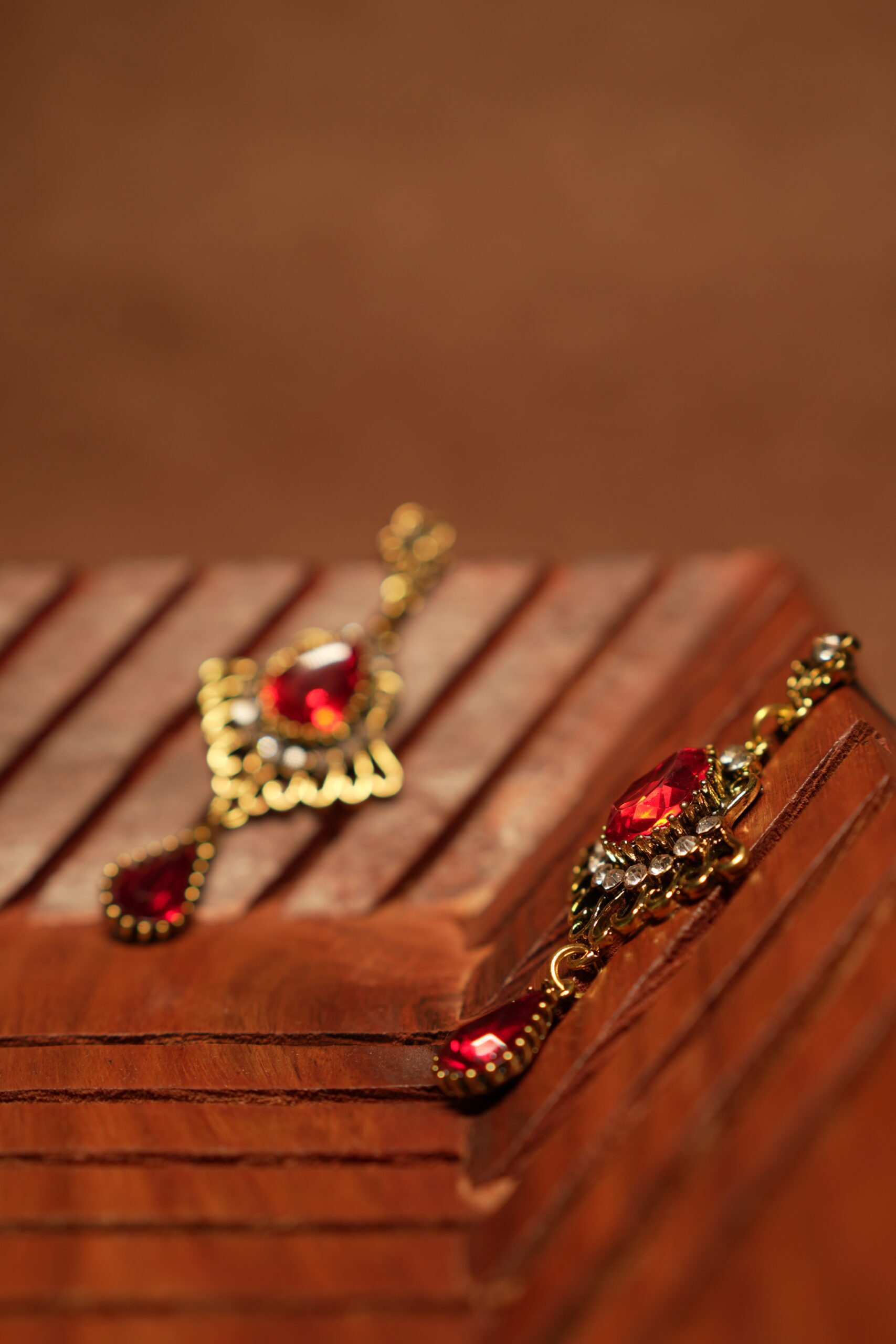 Antique gold floral filigree stud drop earrings with large ruby red teardrop crystal centre stone, white rhinestone accents and red teardrop pendant drop, displayed on wooden surface