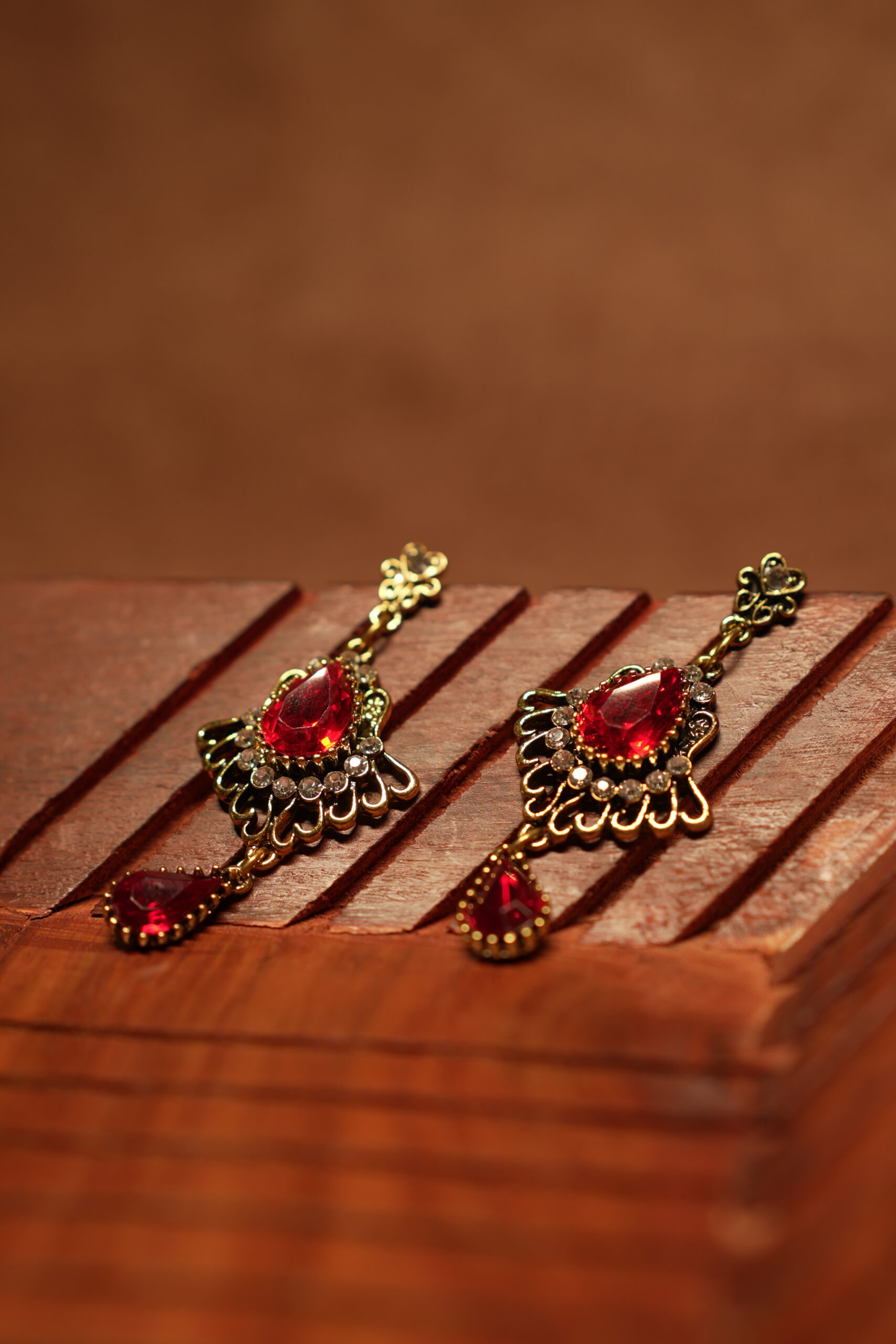 Antique gold floral filigree stud drop earrings with large ruby red teardrop crystal centre stone, white rhinestone accents and red teardrop pendant drop, displayed on wooden surface