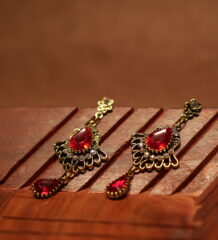 Antique gold floral filigree stud drop earrings with large ruby red teardrop crystal centre stone, white rhinestone accents and red teardrop pendant drop, displayed on wooden surface