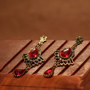 Antique gold floral filigree stud drop earrings with large ruby red teardrop crystal centre stone, white rhinestone accents and red teardrop pendant drop, displayed on wooden surface