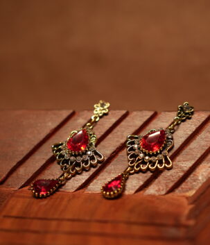 Antique gold floral filigree stud drop earrings with large ruby red teardrop crystal centre stone, white rhinestone accents and red teardrop pendant drop, displayed on wooden surface