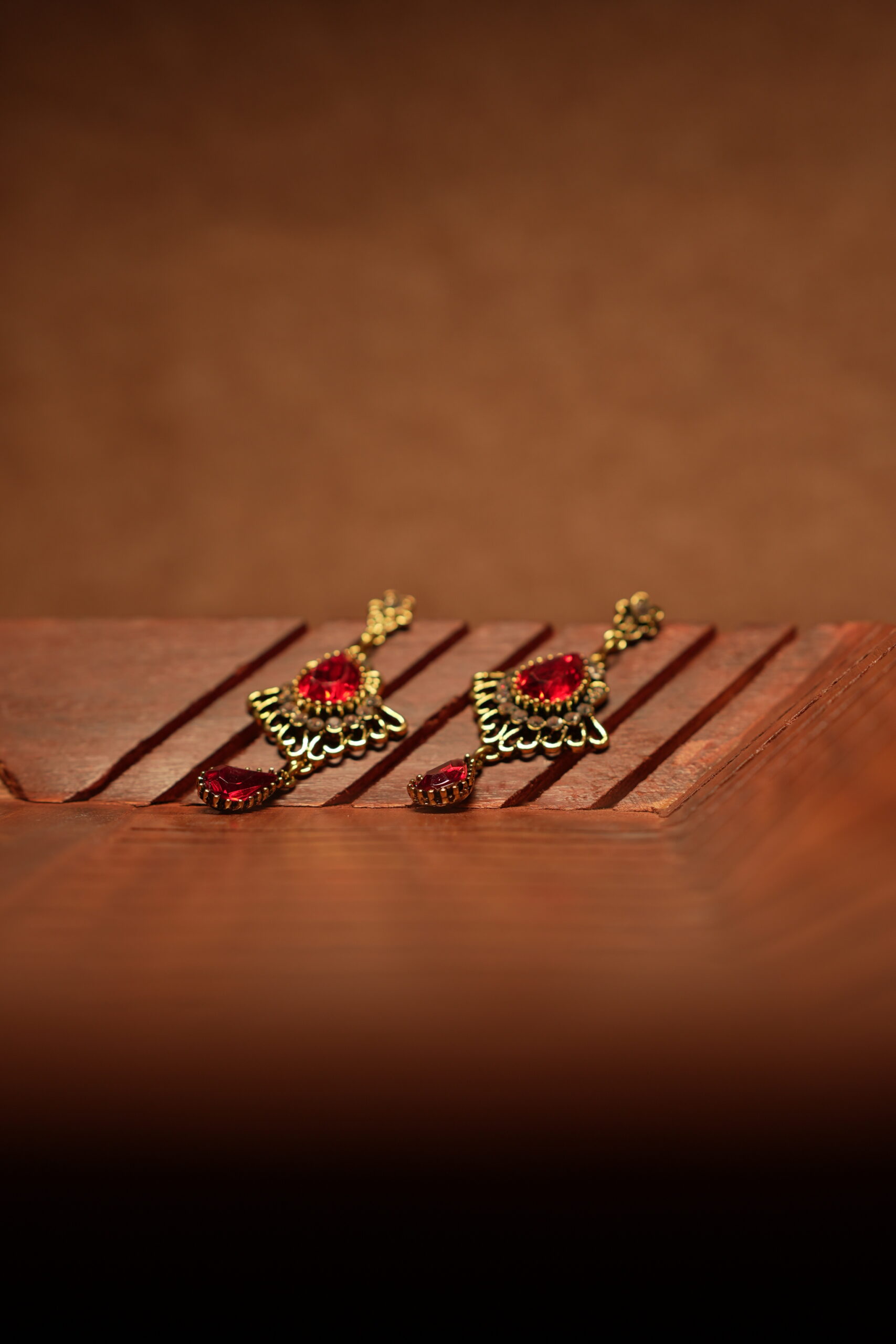 Antique gold floral filigree stud drop earrings with large ruby red teardrop crystal centre stone, white rhinestone accents and red teardrop pendant drop, displayed on wooden surface