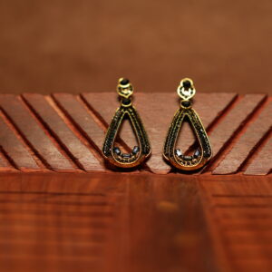 A pair of open teardrop drop earrings with a black crystal-encrusted frame, gold metal border, round black stone stud top, and baguette crystal accents at the base, displayed on a carved wooden surface.