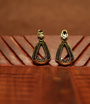 A pair of open teardrop drop earrings with a black crystal-encrusted frame, gold metal border, round black stone stud top, and baguette crystal accents at the base, displayed on a carved wooden surface.