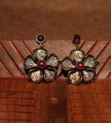 A pair of large antique gold textured five-petal flower drop earrings with a ruby red cabochon centre stone and matching red crystal stud top, displayed on a carved wooden surface.