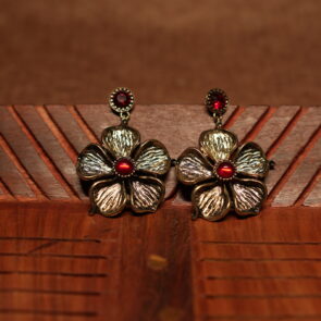 A pair of large antique gold textured five-petal flower drop earrings with a ruby red cabochon centre stone and matching red crystal stud top, displayed on a carved wooden surface.