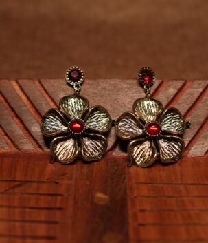A pair of large antique gold textured five-petal flower drop earrings with a ruby red cabochon centre stone and matching red crystal stud top, displayed on a carved wooden surface.