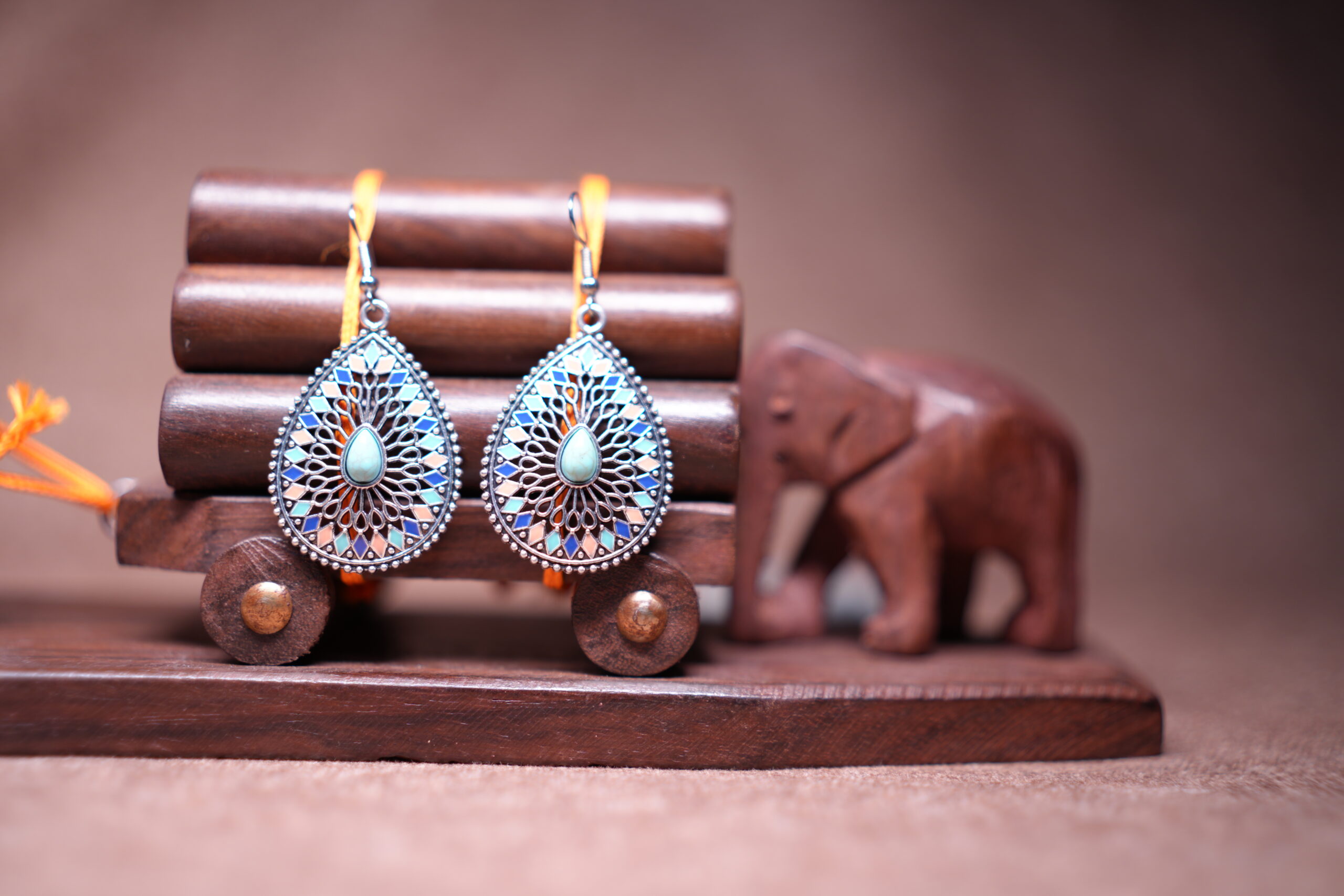 Bohemian teardrop dangle earrings with silver-tone filigree, multicolour enamel mosaic tiles in blue coral and pink, and a turquoise cabochon centre stone, displayed on a wooden jewellery stand