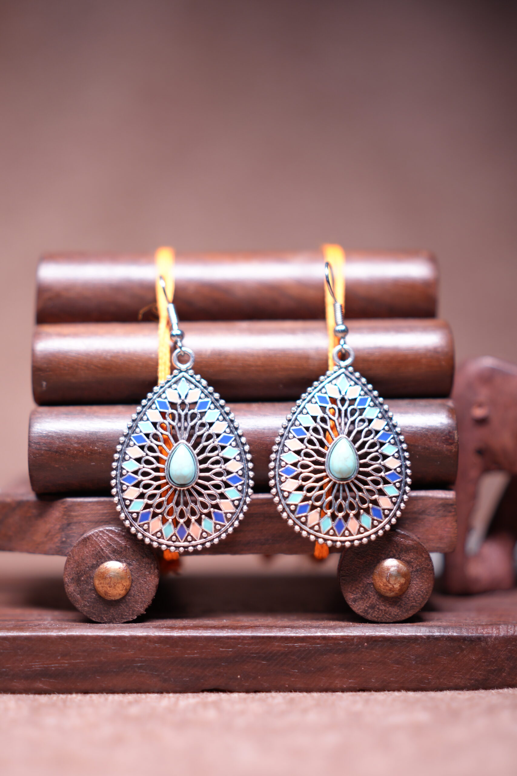Bohemian teardrop dangle earrings with silver-tone filigree, multicolour enamel mosaic tiles in blue coral and pink, and a turquoise cabochon centre stone, displayed on a wooden jewellery stand