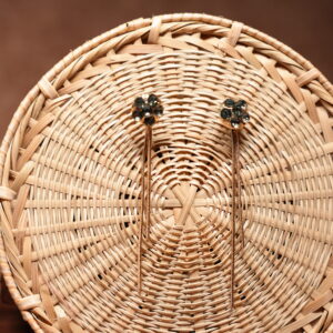 Gold-tone floral dark crystal cluster stud earrings with long multi-strand chain tassel drops, displayed on a round woven rattan basket against a brown background