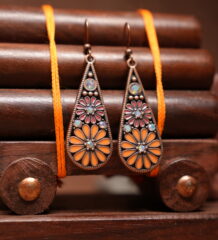 Antique copper-toned teardrop dangle earrings with orange and pink enamel floral motif and opal-effect stone accents, hung on a wooden jewellery stand with a carved elephant figurine