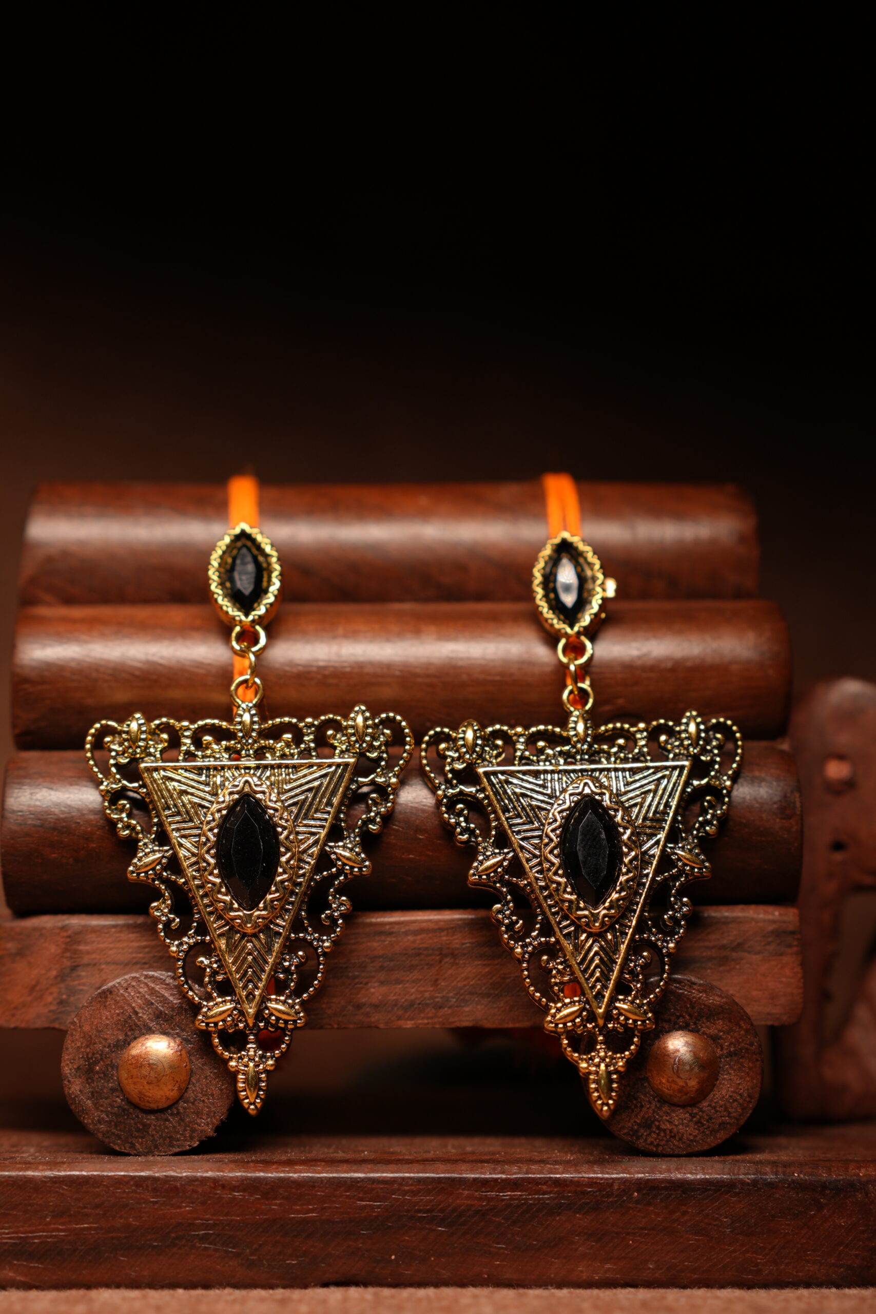 Gold-toned antique triangular drop earrings with black marquise stone, displayed on a wooden jewellery stand with a carved elephant figurine