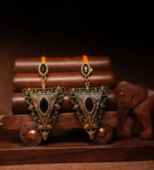 Gold-toned antique triangular drop earrings with black marquise stone, displayed on a wooden jewellery stand with a carved elephant figurine