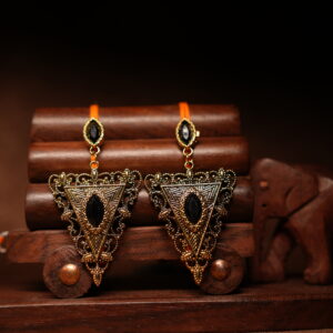 Gold-toned antique triangular drop earrings with black marquise stone, displayed on a wooden jewellery stand with a carved elephant figurine