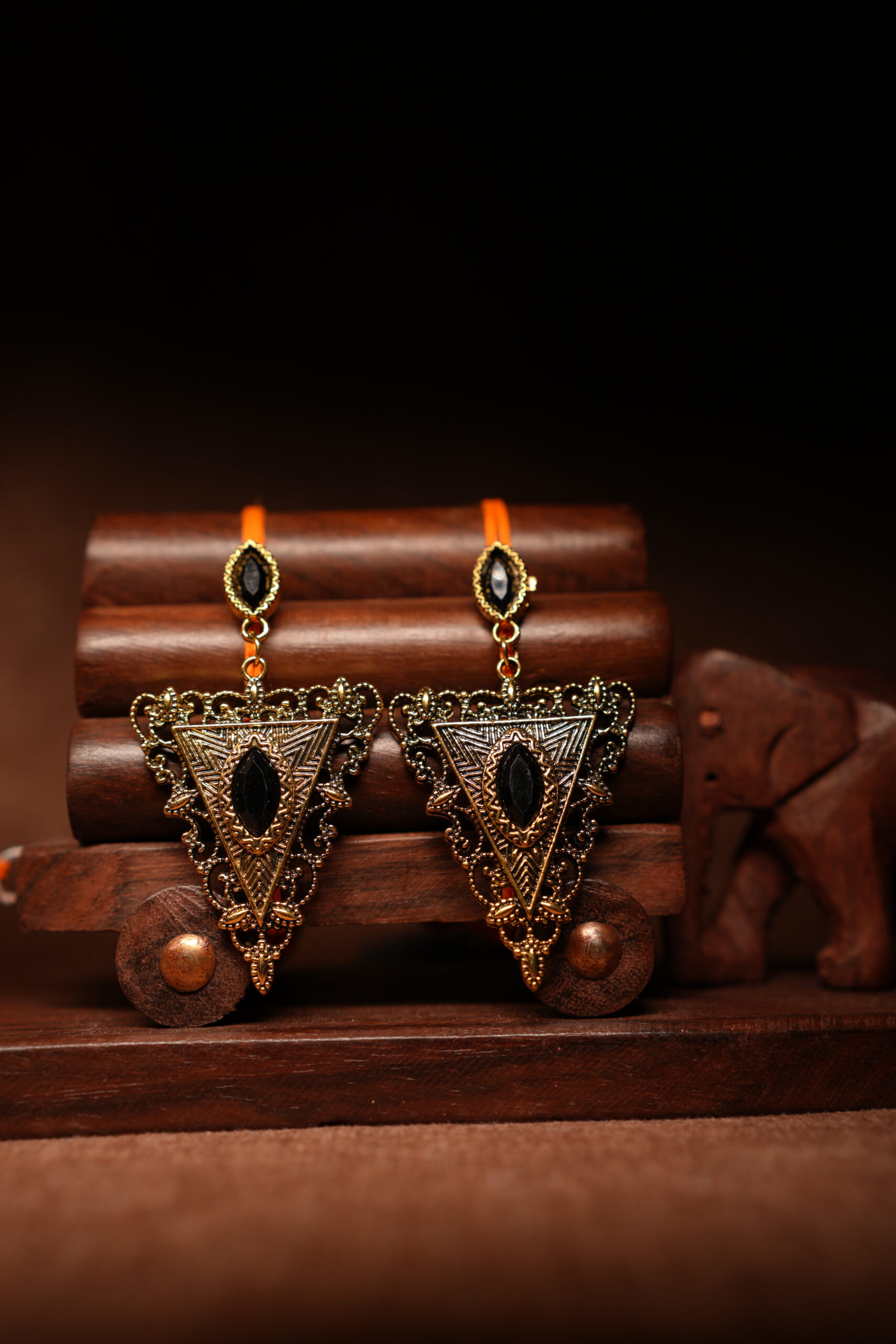 Gold-toned antique triangular drop earrings with black marquise stone, displayed on a wooden jewellery stand with a carved elephant figurine