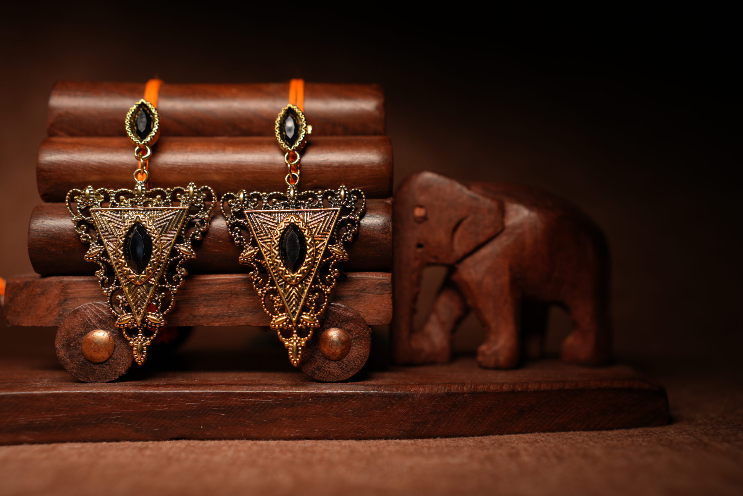 Gold-toned antique triangular drop earrings with black marquise stone, displayed on a wooden jewellery stand with a carved elephant figurine