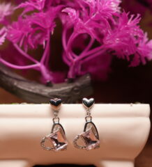 Silver-tone double heart drop earrings with clear square-cut crystal pendant set in a CZ-studded open heart frame, displayed on a white ceramic bowl