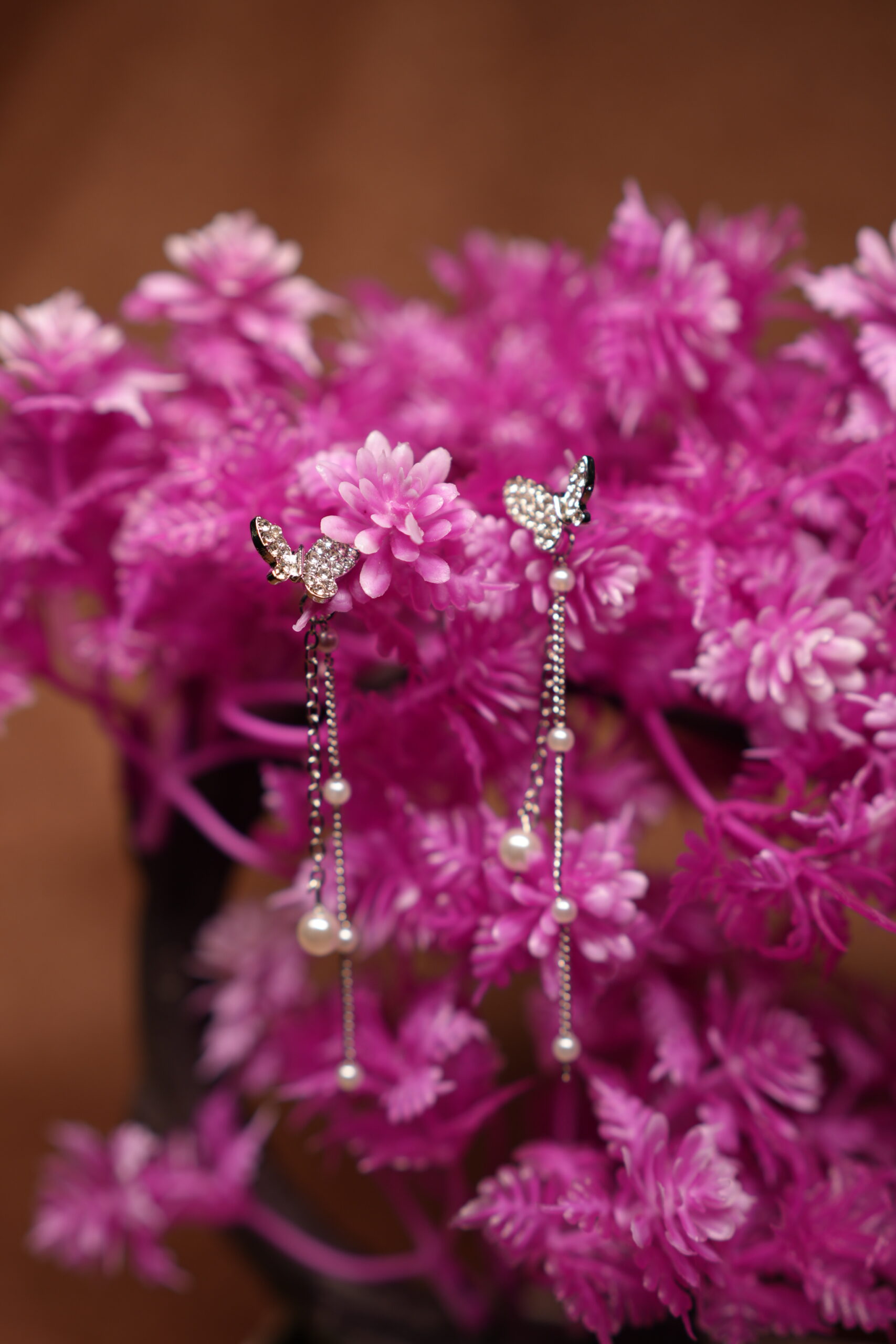 Crystal butterfly stud earrings with silver chain and faux pearl drops displayed on pink artificial flower tree – D2Dazzle fashion jewellery India