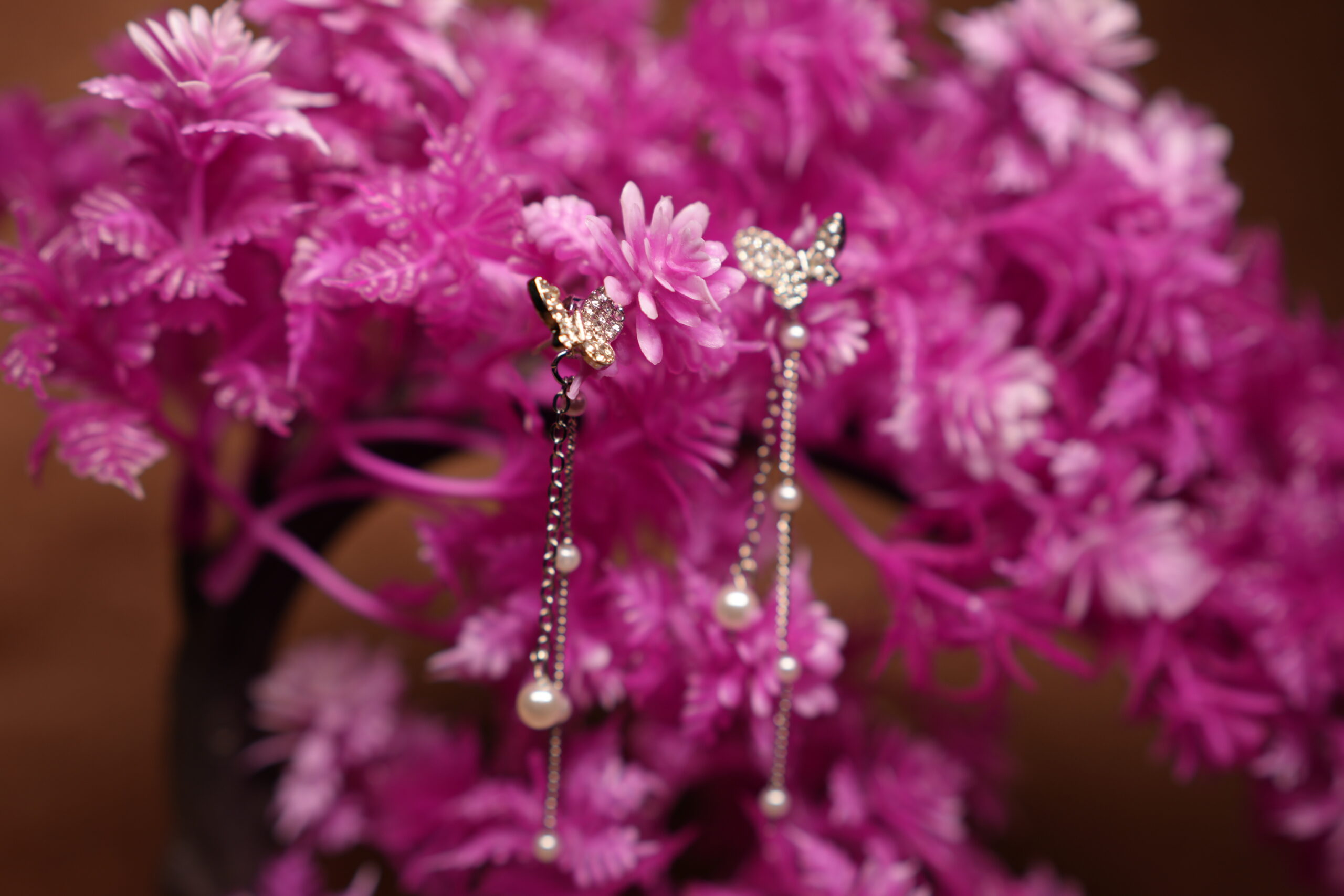 Crystal butterfly stud earrings with silver chain and faux pearl drops displayed on pink artificial flower tree – D2Dazzle fashion jewellery India