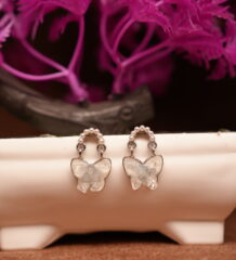 Silver pearl hoop earrings with clear crystal butterfly pendant drop displayed on white ceramic stand with pink flowers – D2Dazzle fashion jewellery India