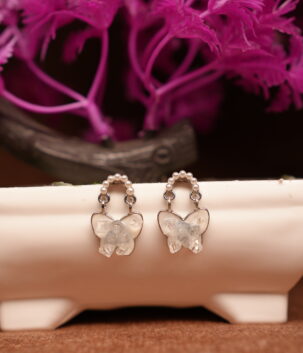 Silver pearl hoop earrings with clear crystal butterfly pendant drop displayed on white ceramic stand with pink flowers – D2Dazzle fashion jewellery India