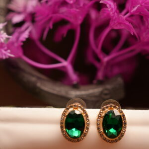 Emerald green oval halo stud earrings with gold-tone rhinestone crystal border displayed on white ceramic stand with pink flowers – D2Dazzle fashion jewellery India