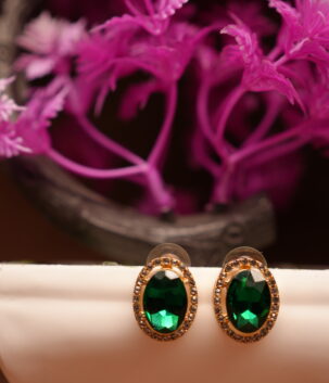 Emerald green oval halo stud earrings with gold-tone rhinestone crystal border displayed on white ceramic stand with pink flowers – D2Dazzle fashion jewellery India