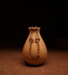 Gold crystal twist tassel drop earrings with pavé rhinestone knot and multi-strand snake chain, displayed on ceramic vase — D2Dazzle