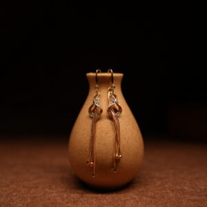 Gold crystal twist tassel drop earrings with pavé rhinestone knot and multi-strand snake chain, displayed on ceramic vase — D2Dazzle