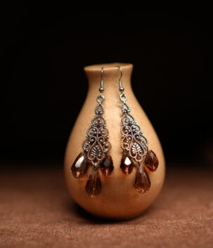 Silver filigree chandelier earrings with three amber crystal teardrop drops displayed on golden ceramic vase with dark background – D2Dazzle antique fashion jewellery India