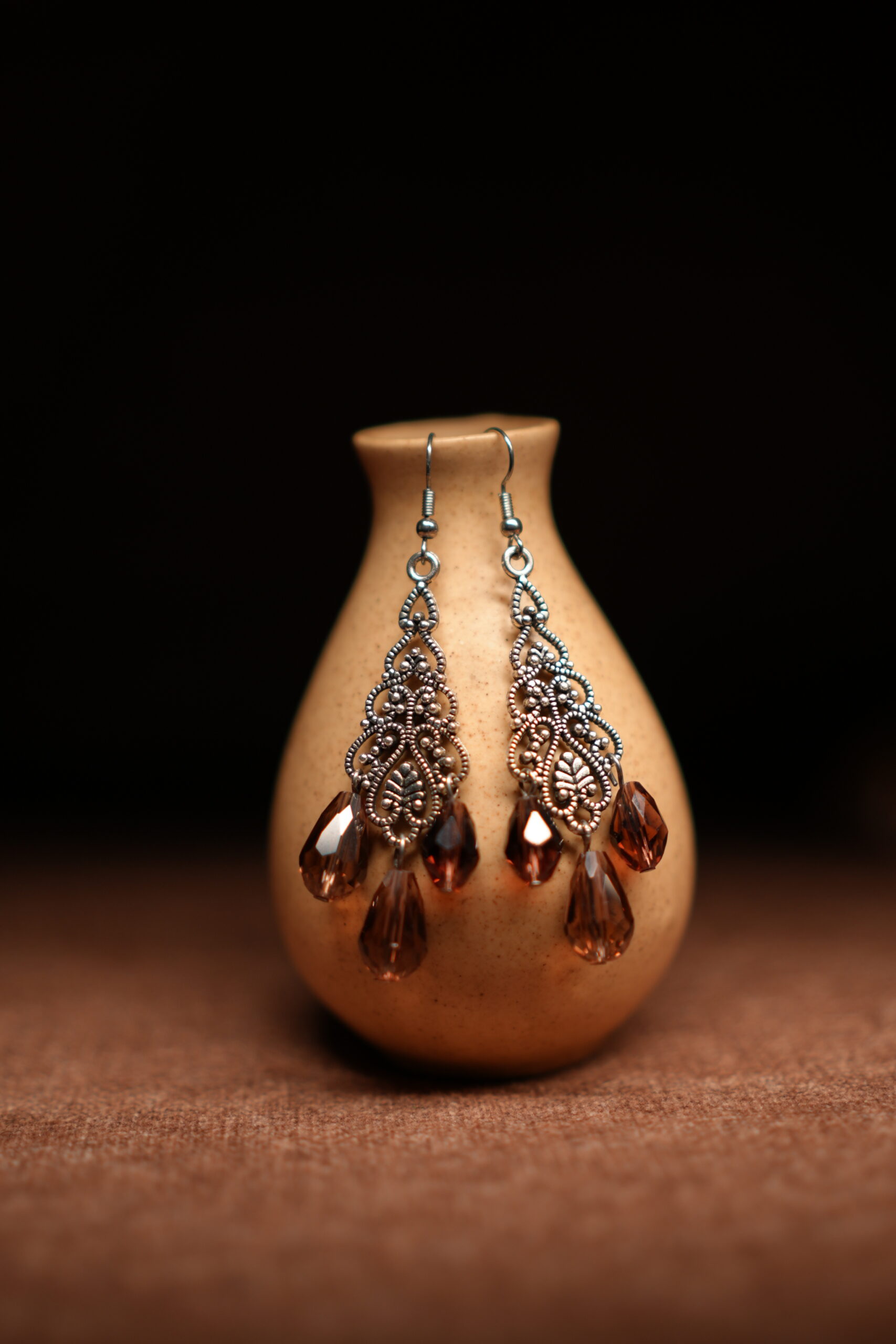 Silver filigree chandelier earrings with three amber crystal teardrop drops displayed on golden ceramic vase with dark background – D2Dazzle antique fashion jewellery India