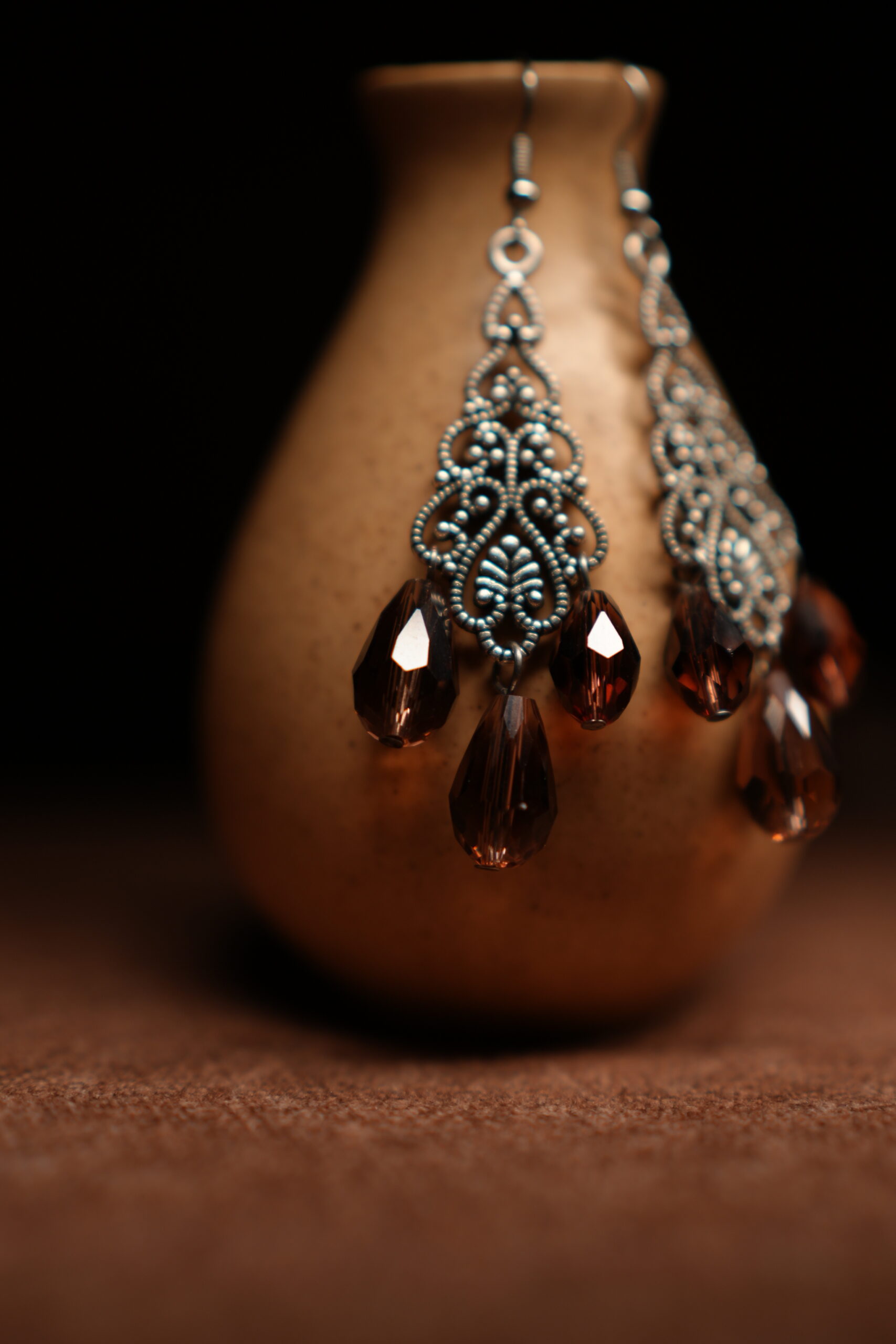 Silver filigree chandelier earrings with three amber crystal teardrop drops displayed on golden ceramic vase with dark background – D2Dazzle antique fashion jewellery India