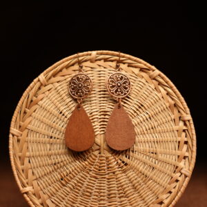 A pair of copper-tone filigree mandala disc and natural walnut wood teardrop drop earrings on French hooks, displayed against a round woven rattan disc on a warm brown background.