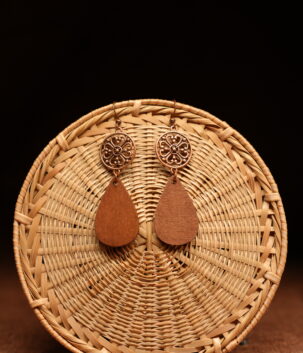 A pair of copper-tone filigree mandala disc and natural walnut wood teardrop drop earrings on French hooks, displayed against a round woven rattan disc on a warm brown background.