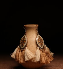 A pair of ivory and gold lotus enamel marquise-shaped drop earrings with five alternating ivory cream and champagne gold thread tassels, displayed on a speckled beige ceramic vase against a dark background.