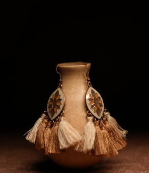 A pair of ivory and gold lotus enamel marquise-shaped drop earrings with five alternating ivory cream and champagne gold thread tassels, displayed on a speckled beige ceramic vase against a dark background.