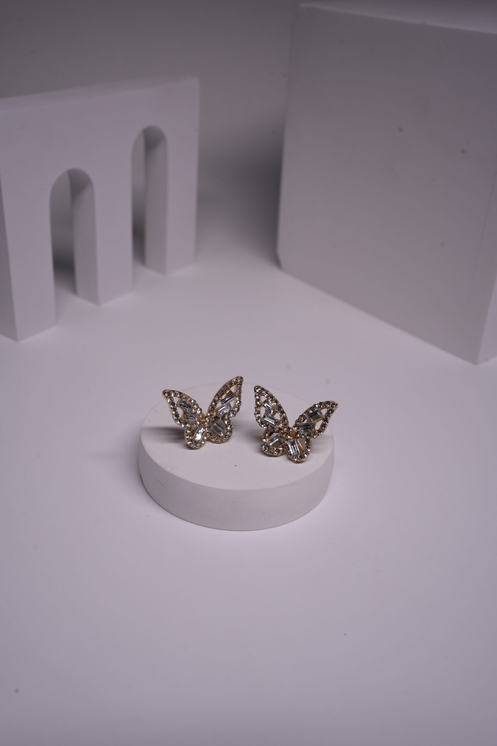 Gold-toned baguette and round crystal butterfly stud earrings displayed on a white cylindrical prop