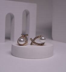 Gold-toned crystal wishbone pearl stud earrings displayed on a white cylindrical prop