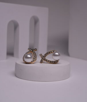 Gold-toned crystal wishbone pearl stud earrings displayed on a white cylindrical prop