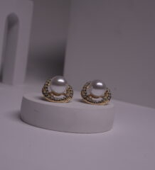 Gold-toned faux pearl stud earrings with crystal rhinestone halo displayed on a white cylindrical prop