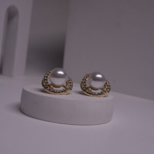 Gold-toned faux pearl stud earrings with crystal rhinestone halo displayed on a white cylindrical prop