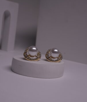 Gold-toned faux pearl stud earrings with crystal rhinestone halo displayed on a white cylindrical prop