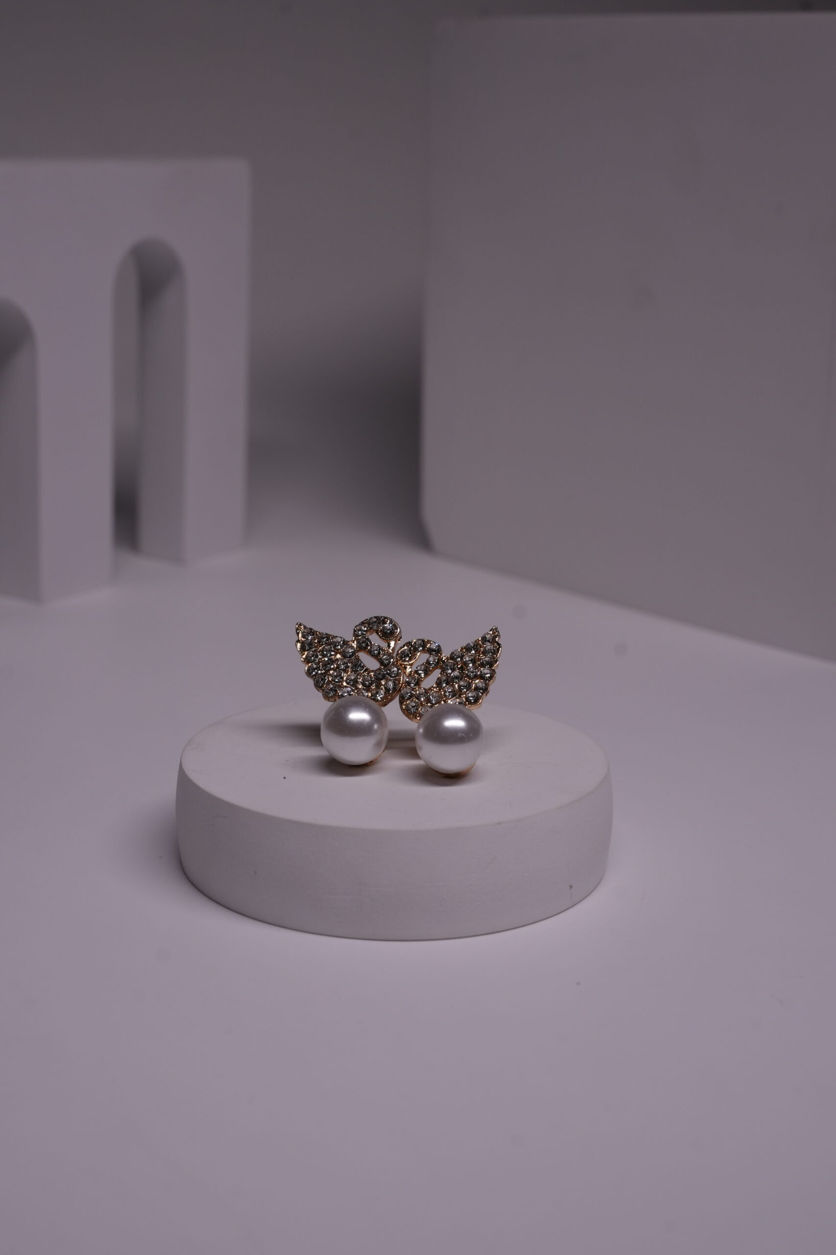 Gold-toned crystal butterfly stud earrings with faux pearl drops displayed on a white cylindrical prop