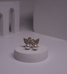 Gold-toned crystal butterfly stud earrings with faux pearl drops displayed on a white cylindrical prop