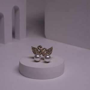 Gold-toned crystal butterfly stud earrings with faux pearl drops displayed on a white cylindrical prop