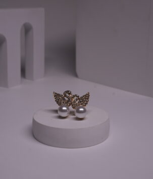 Gold-toned crystal butterfly stud earrings with faux pearl drops displayed on a white cylindrical prop