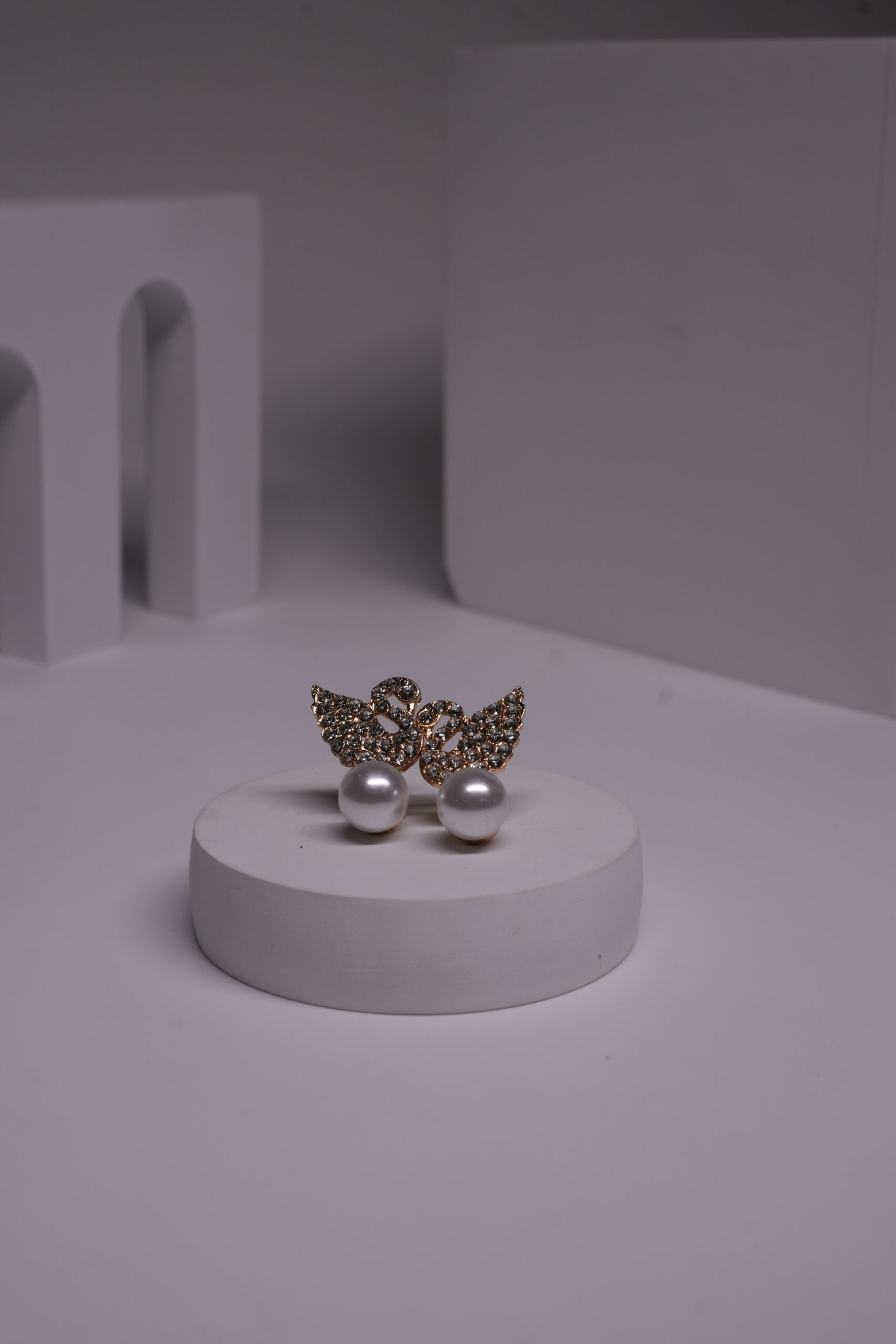 Gold-toned crystal butterfly stud earrings with faux pearl drops displayed on a white cylindrical prop