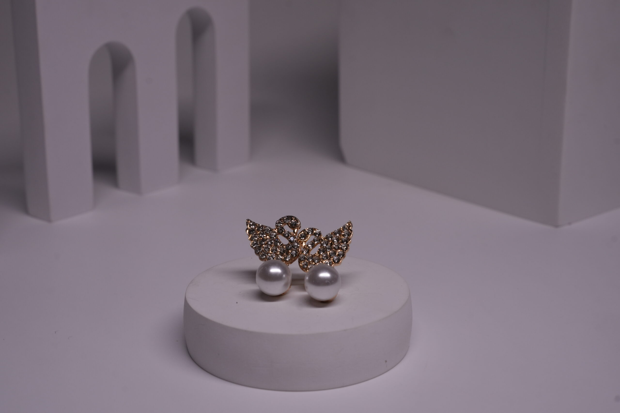 Gold-toned crystal butterfly stud earrings with faux pearl drops displayed on a white cylindrical prop